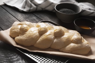 Raw braided bread and ingredients on black wooden table, closeup. Traditional Shabbat challah