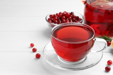 Photo of Tasty hot cranberry tea in glass cup and fresh berries on white wooden table