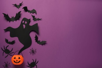 Flat lay composition with paper ghost, bats and plastic pumpkin basket on purple background, space for text. Halloween celebration