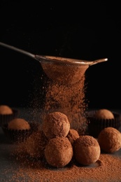 Photo of Tasty chocolate truffles powdered with cocoa from sieve on grey table
