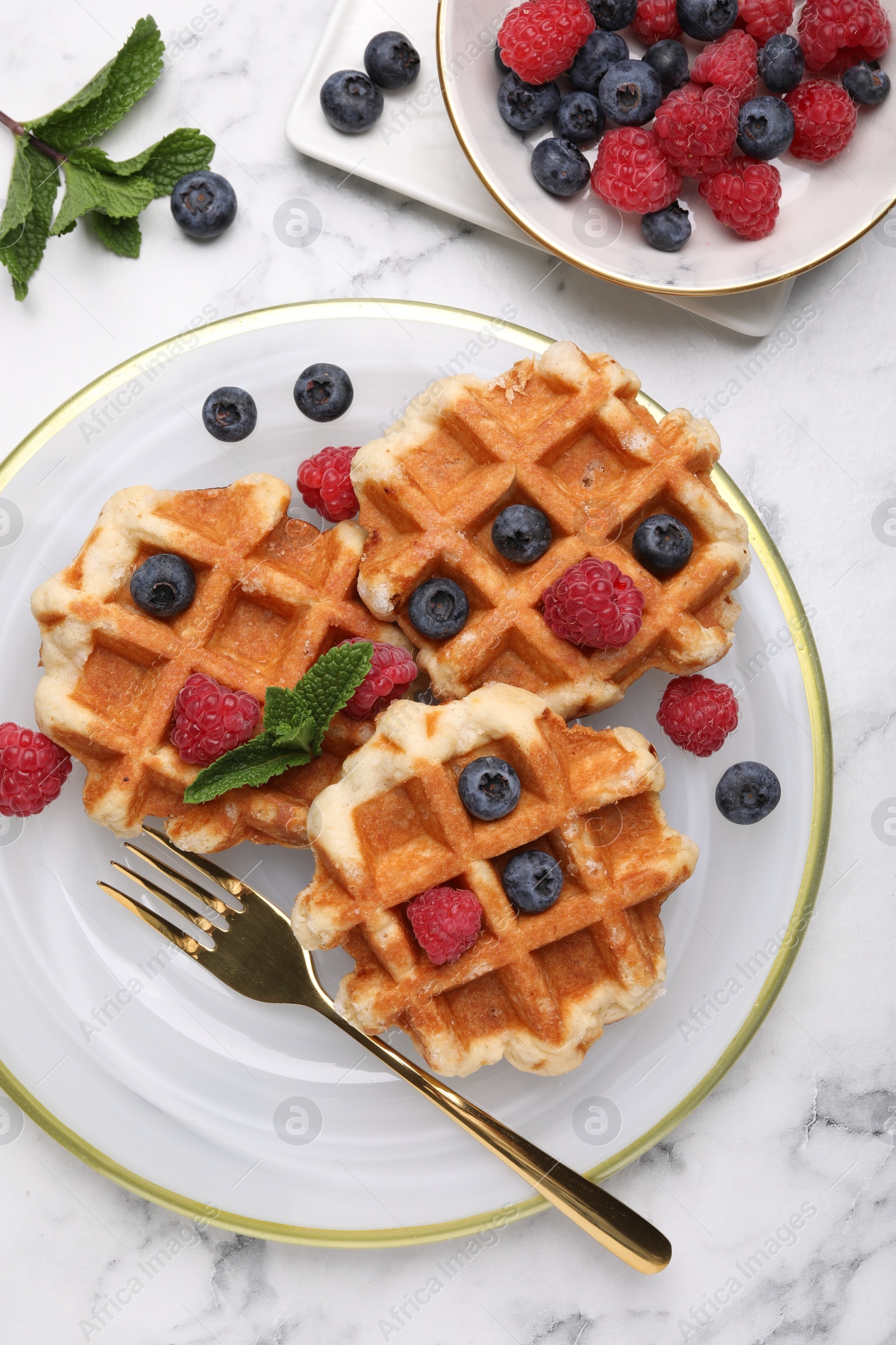 Photo of Delicious Belgian waffles with fresh berries and mint on white marble table, flat lay