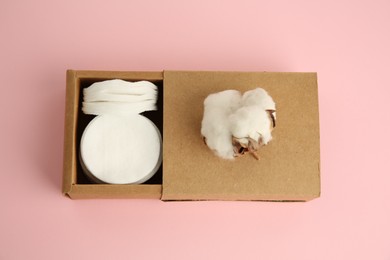 Photo of Cardboard box with cotton pads and flower on pink background, top view