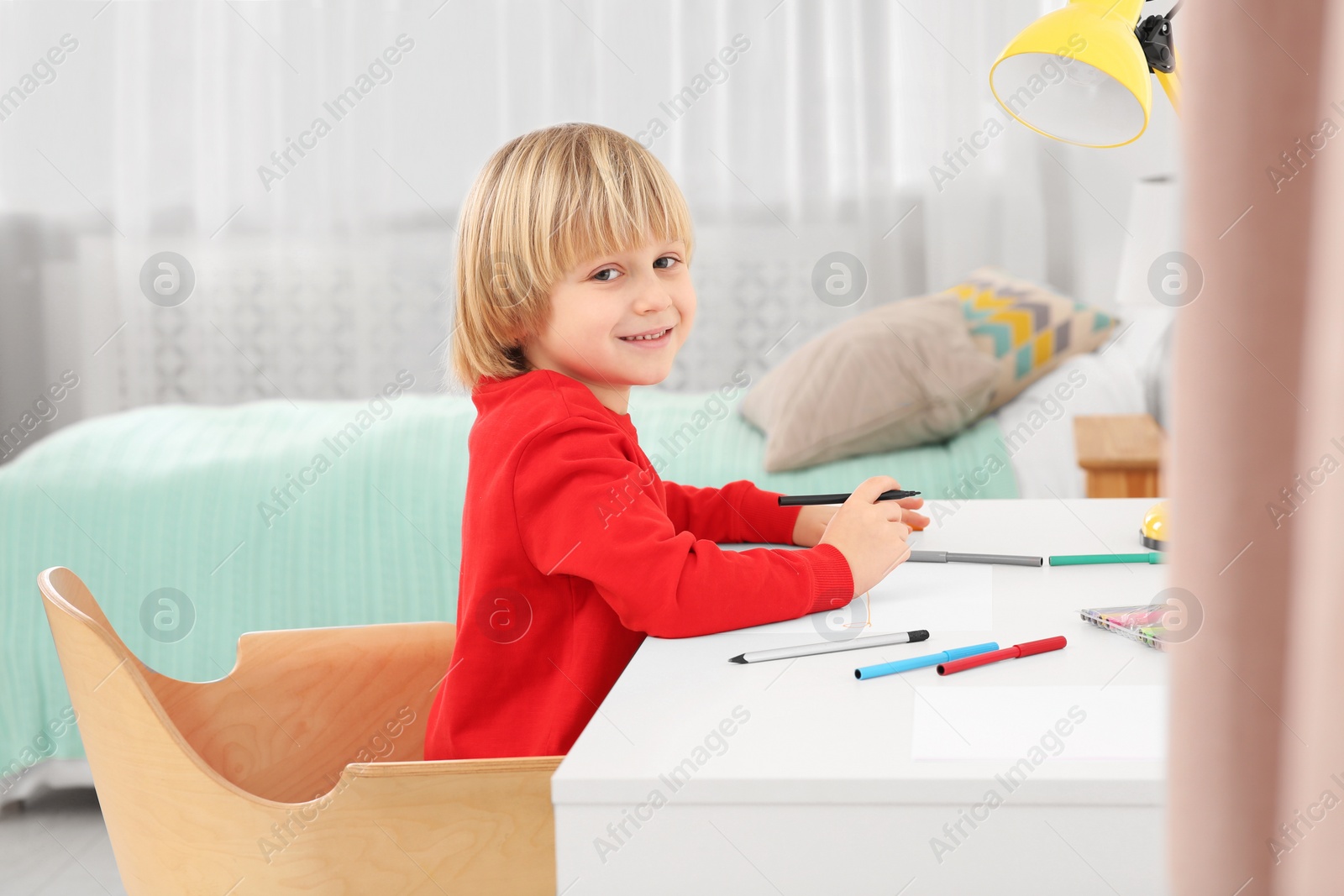 Photo of Little boy drawing at desk in room. Home workplace