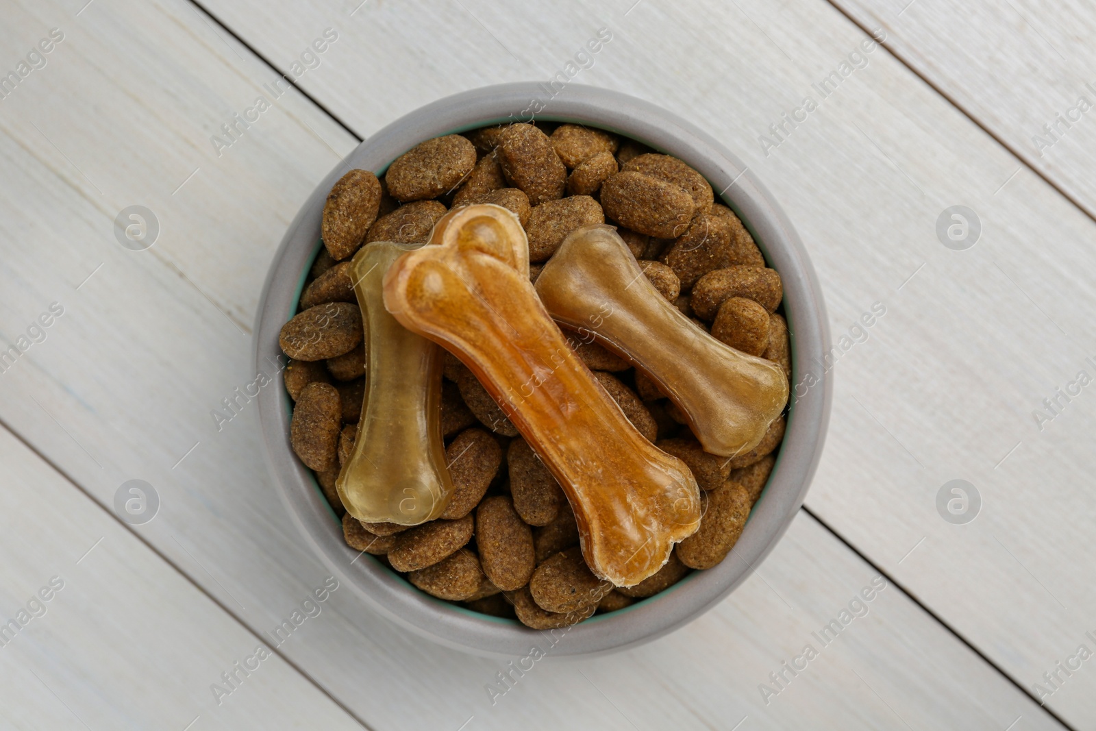 Photo of Dry dog food and treats (chew bones) on white wooden floor, top view