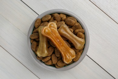 Dry dog food and treats (chew bones) on white wooden floor, top view