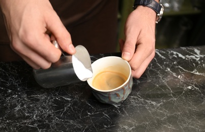 Barista adding milk to coffee at table, closeup