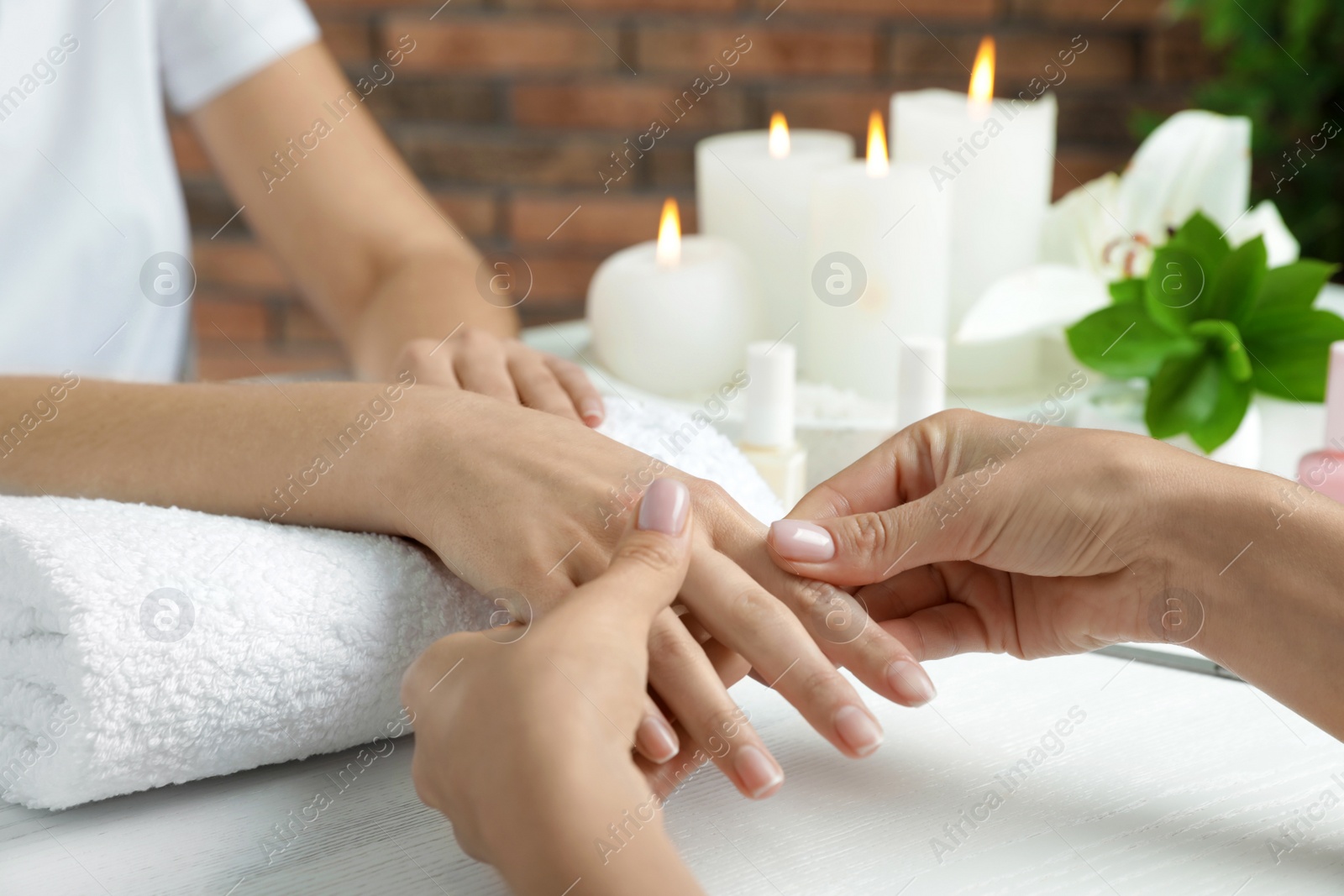 Photo of Cosmetologist massaging client's hand at table in spa salon, closeup