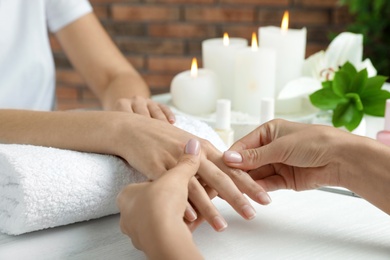 Photo of Cosmetologist massaging client's hand at table in spa salon, closeup