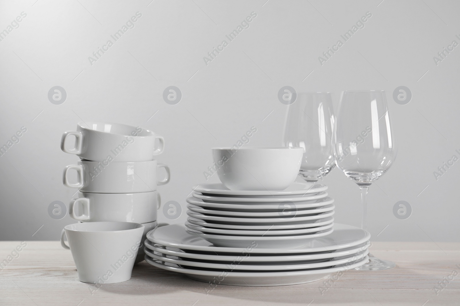 Photo of Set of clean dishware and glasses on white wooden table against light background