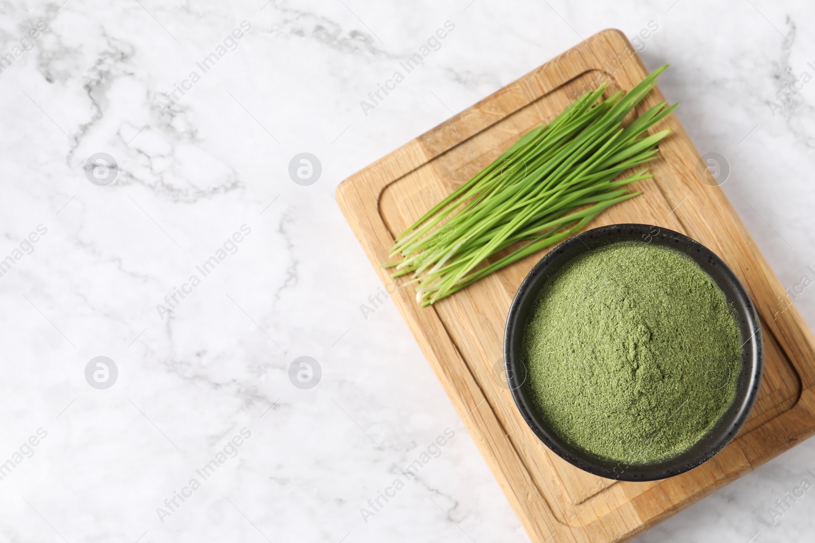 Photo of Wheat grass powder in bowl and fresh sprouts on white marble table, top view. Space for text