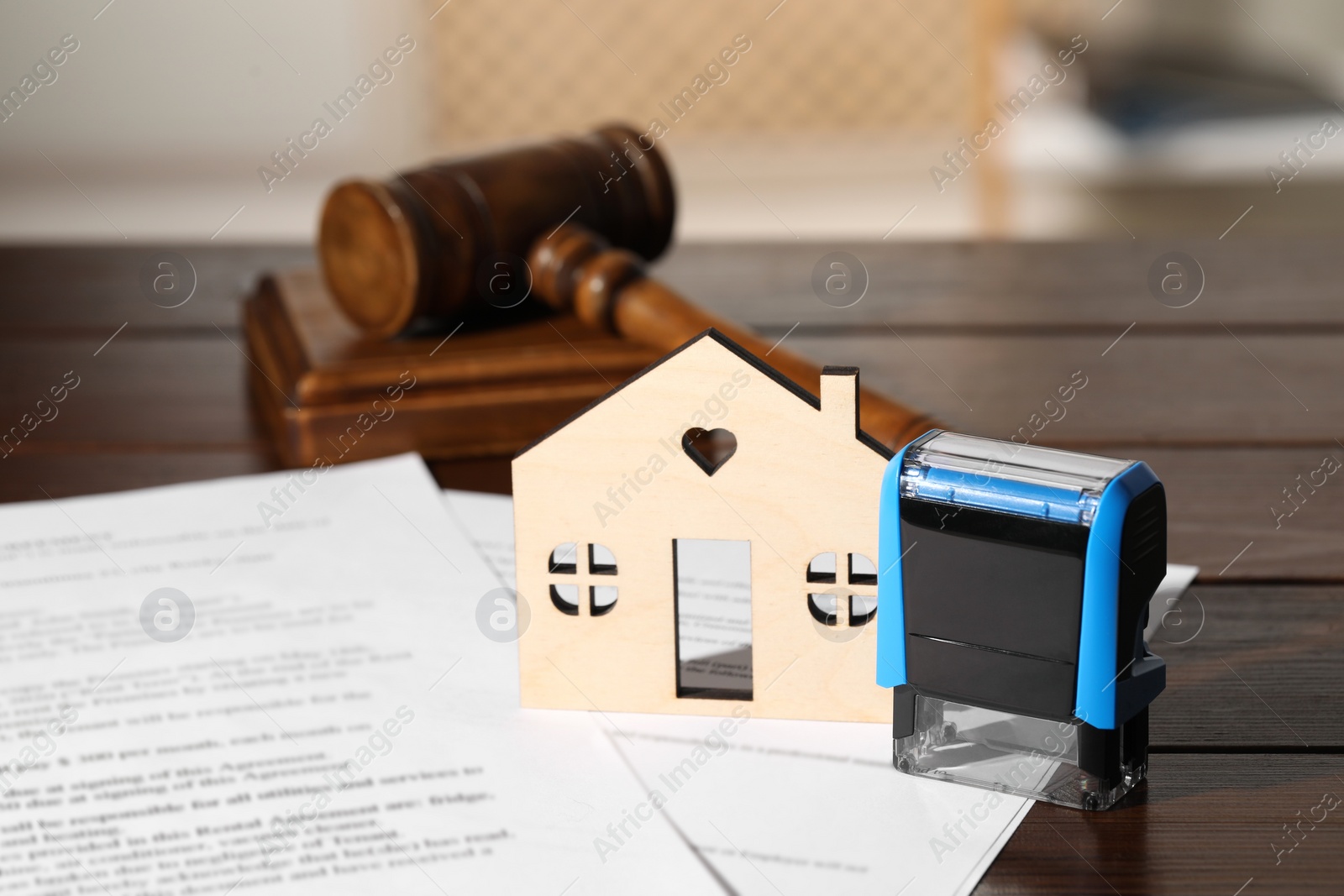 Photo of Notary contract. Figure of house, stamp, documents and gavel on wooden table