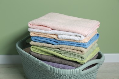 Photo of Plastic laundry basket with clean terry towels on floor near light green wall, closeup