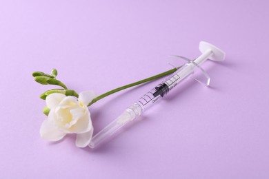 Photo of Cosmetology. Medical syringe and freesia flower on violet background
