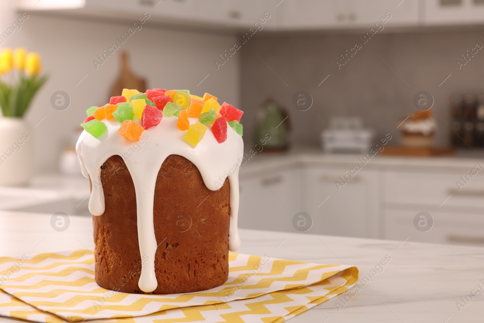 Photo of Delicious Easter cake decorated with pieces of candied fruits on white table in kitchen. Space for text