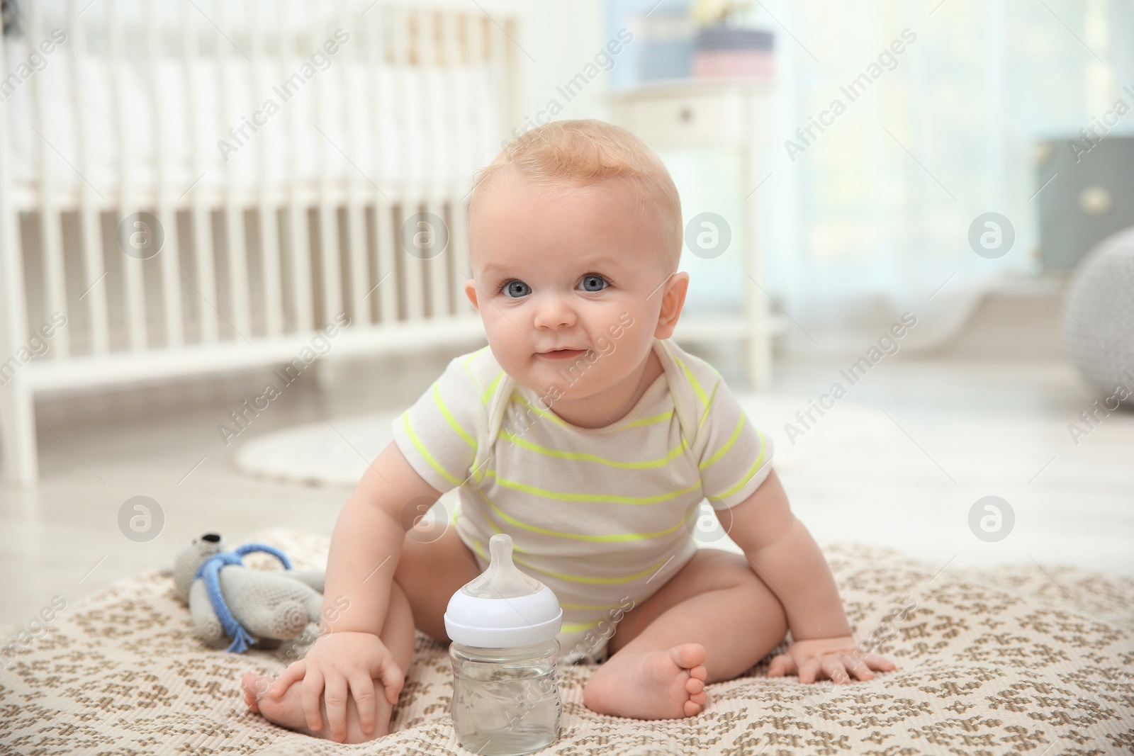 Photo of Cute baby with bottle sitting on floor in room