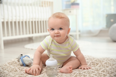 Cute baby with bottle sitting on floor in room