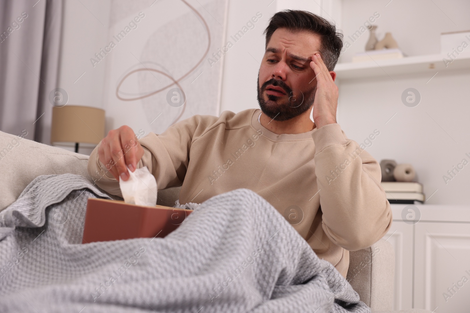 Photo of Sick man with tissues on sofa at home. Cold symptoms