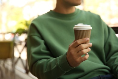 Man with takeaway coffee cup in outdoor cafe, closeup