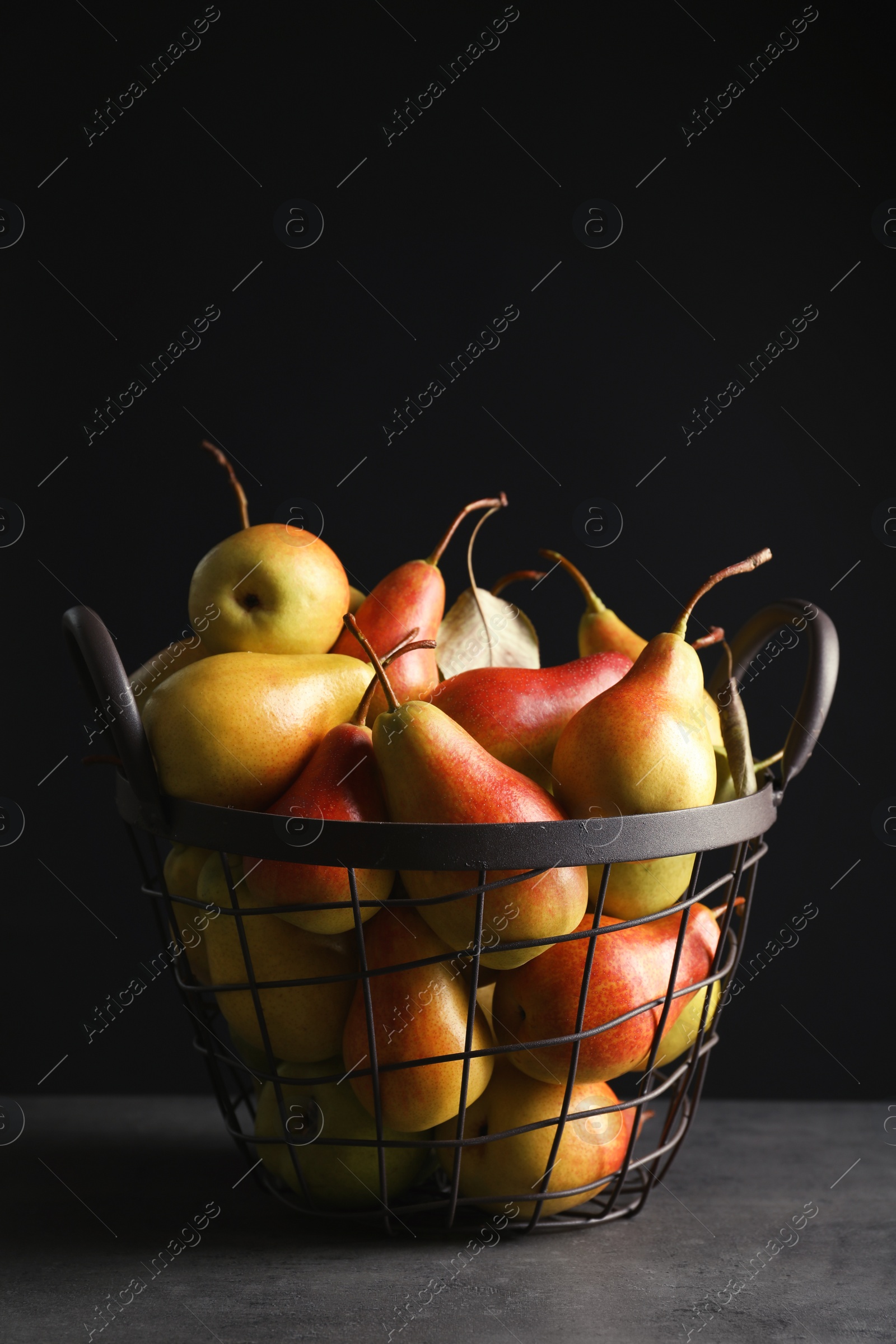 Photo of Basket with ripe pears on table against black background. Space for text