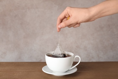 Photo of Woman brewing tea with bag in cup on table against color background