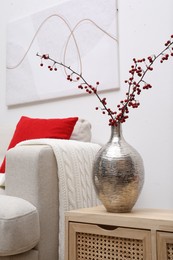 Hawthorn branches with red berries on wooden commode in living room