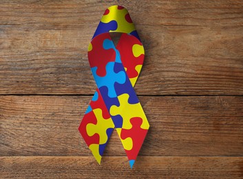 Image of World Autism Awareness Day. Colorful puzzle ribbon on wooden background, top view