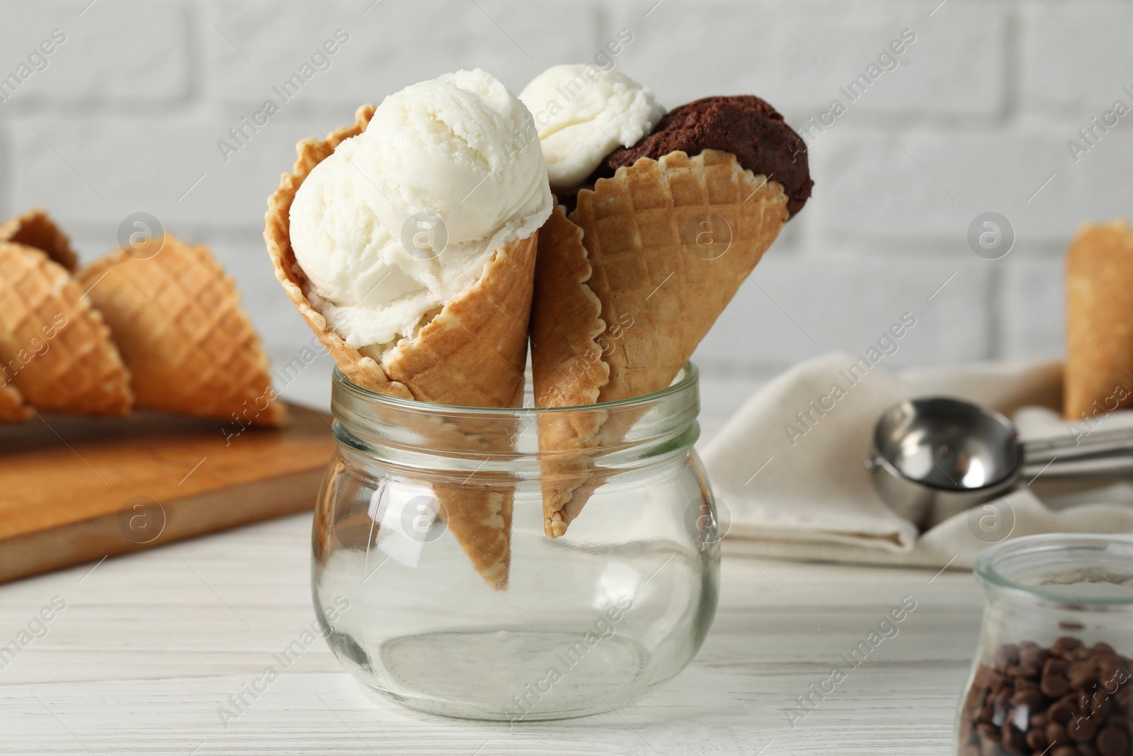 Photo of Ice cream scoops in wafer cones on white wooden table against brick wall