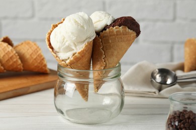 Photo of Ice cream scoops in wafer cones on white wooden table against brick wall