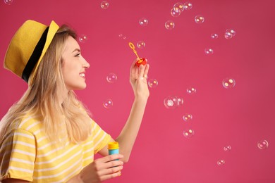 Photo of Young woman blowing soap bubbles on pink background, space for text