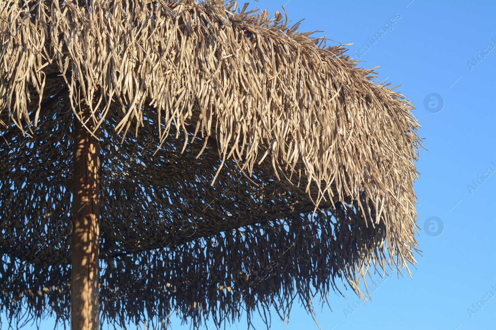 Photo of Beautiful straw beach umbrella against blue sky, closeup