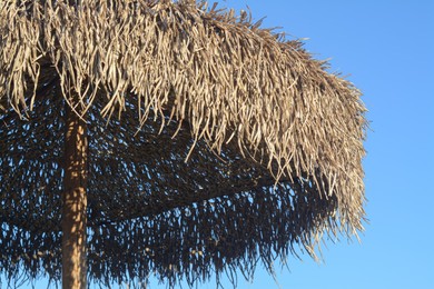 Beautiful straw beach umbrella against blue sky, closeup