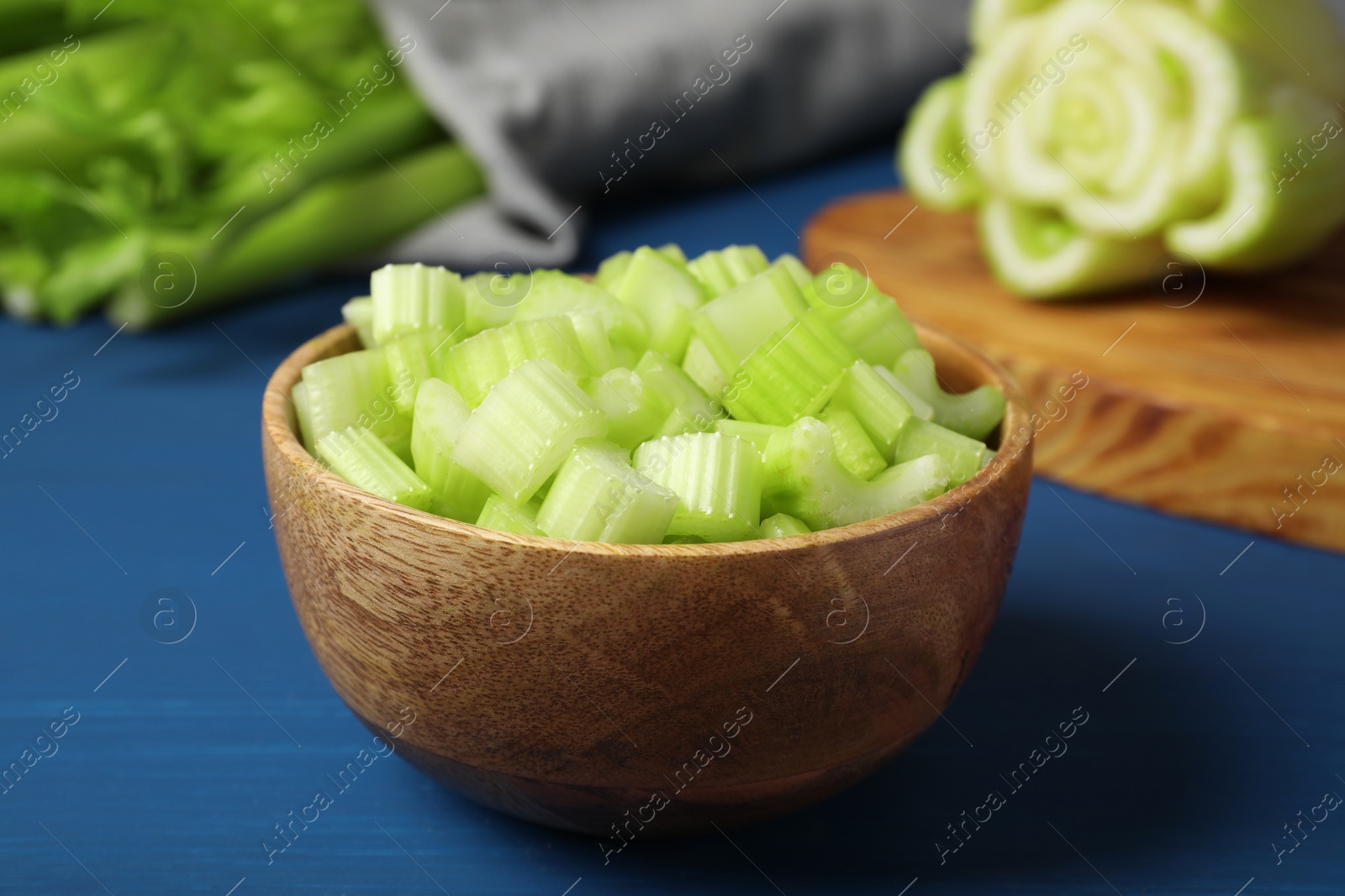 Photo of Bowl of fresh cut celery on blue wooden table, closeup