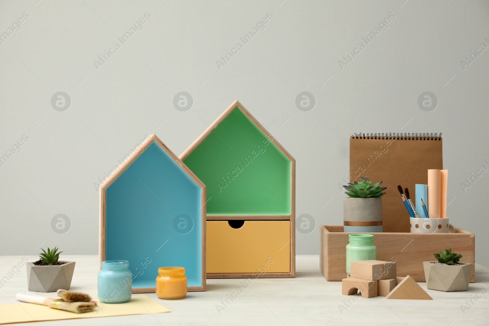 Photo of Composition with house shaped shelves and jars of paints on white table. Interior elements