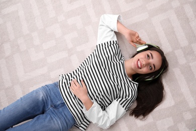 Photo of Young woman in headphones enjoying music on floor, top view