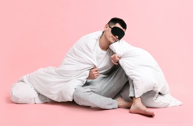 Photo of Man in pyjama and sleep mask wrapped in blanket on pink background