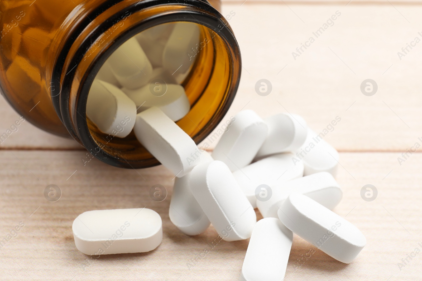 Photo of Bottle and vitamin pills on wooden table, closeup