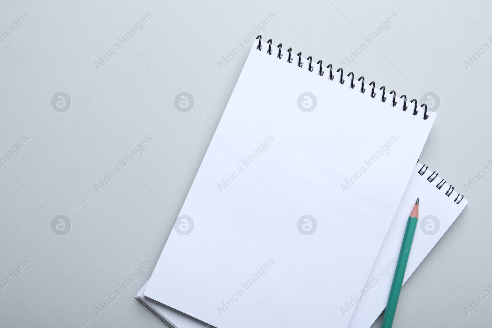 Photo of Notebooks and pencil on light grey background, top view. Space for text