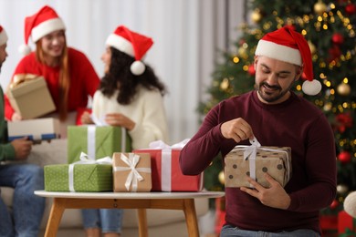 Christmas celebration in circle of friends. Happy man opening gift at home, selective focus