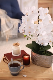 Photo of Beautiful white orchids, books, cup of tea and candles on table in room. Interior design