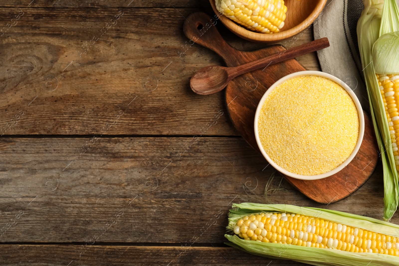 Photo of Cornmeal in bowl and fresh cobs on wooden table, flat lay. Space for text