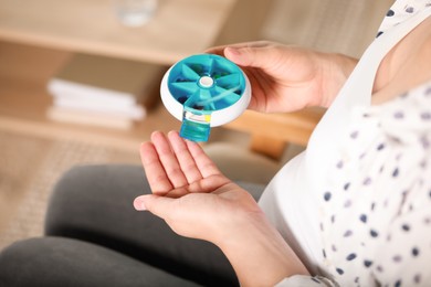 Photo of Pregnant woman taking pill from container indoors, closeup