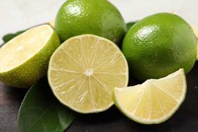 Photo of Whole and cut fresh limes on black board, closeup