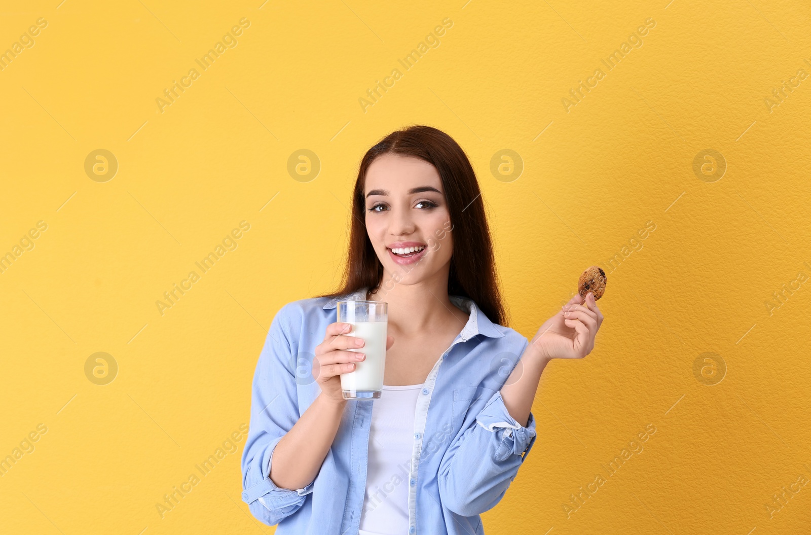 Photo of Beautiful young woman drinking milk with cookie on color background