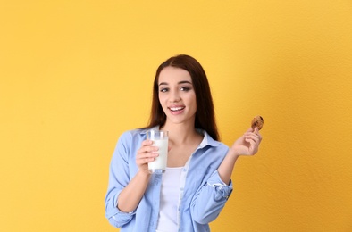 Beautiful young woman drinking milk with cookie on color background