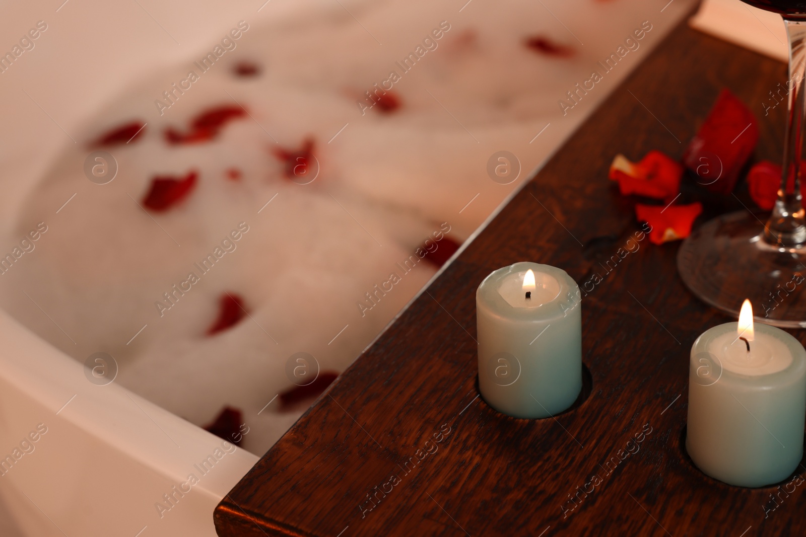 Photo of Wooden board with burning candles on bath tub, closeup