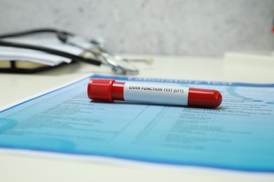 Liver Function Test. Tube with blood sample and form on white table, closeup