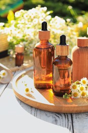 Photo of Bottles of essential oil and flowers on white wooden table outdoors