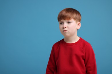 Portrait of sad little boy on light blue background, space for text