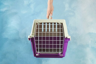 Photo of Woman holding pet carrier against light blue wall, closeup. Space for text