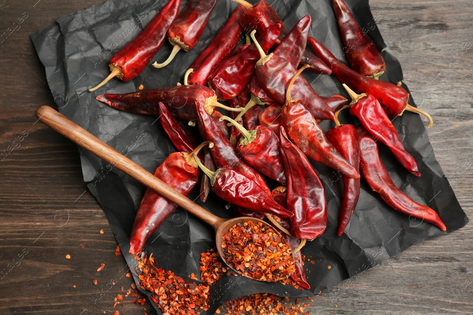 Photo of Spoon with chili pepper powder and pods on wooden table